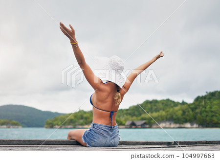 Island, ocean and happy woman relax on deck for holiday, summer vacation and weekend getaway in Maldives. Luxury resort, tropical beach and female person with arms up for tourism, sea and adventure 104997663