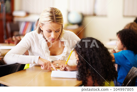Teacher, teaching and child learning to write at school for education, knowledge or development. Woman with girl student for solution, notebook and pencil at a classroom desk with support and help Teacher, teaching and child learning to write at school for education, knowledge or development. Woman with girl student for solution, notebook and pencil at a classroom desk with support and help 104997805