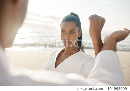 Block, then strike. Cropped shot of two young martial artists practicing karate on the beach. 104998009