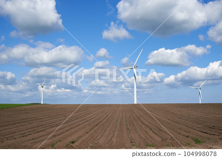 Wind turbines and environmental infrastructure isolated against blue sky with copy space on an empty energy farm. Propellers converting sustainable energy into electric power in remote and rural area 104998078
