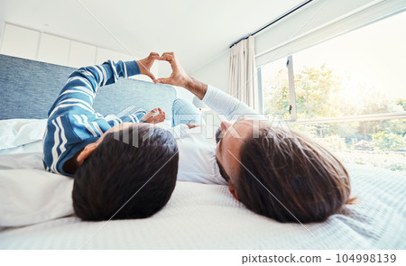 Heart shape, father and son on bed, quality time and happiness on break, relax and bonding together. Family, dad and boy in bedroom, sign for love and resting with joy, carefree and loving in morning 104998139