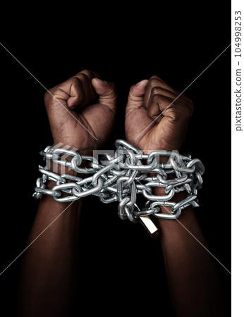 Chain, hands and prisoner of slavery isolated in studio on a black background. Chained, slave and hand of person in bondage, hostage or criminal in jail after arrest for crime, law and punishment. 104998253