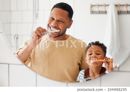 Brushing teeth, father and child in a home bathroom for dental health and wellness with smile. Face of a man and african boy kid learning to clean mouth with a toothbrush and mirror for oral hygiene Brushing teeth, father and child in a home bathroom for dental health and wellness with smile. Face of a man and african boy kid learning to clean mouth with a toothbrush and mirror for oral hygiene 104998295