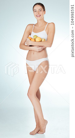 Eat right, feel light. Studio shot of an attractive and fit young woman holding fruit against a blue background. Eat right, feel light. Studio shot of an attractive and fit young woman holding fruit against a blue background. 104998591