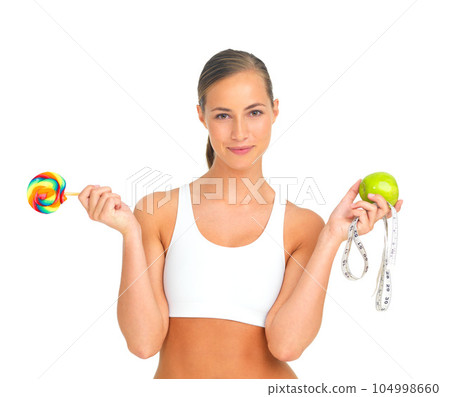 Lollipop, apple and fitness choice of woman in studio isolated on a white background. Face portrait, healthy diet decision and young female model holding candy, fruit vitamins and measuring tape. Lollipop, apple and fitness choice of woman in studio isolated on a white background. Face portrait, healthy diet decision and young female model holding candy, fruit vitamins and measuring tape. 104998660