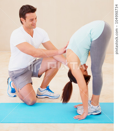 Man, yoga and personal trainer helping woman in body stretching for fitness, exercise or workout at gym. Male yogi instructor, coach or mentor assisting female in warm up stretch or pose on floor mat 104998734