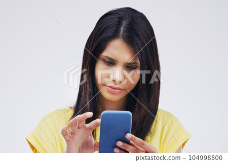Serious, phone and woman typing in studio isolated on white background for social media. Mobile, cellphone and female person texting, networking or email, web scroll or browsing online messaging app. 104998800