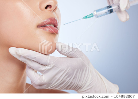 Mouth, botox and plastic surgery with hands on the face of a woman for cosmetic surgery in studio on a blue background. Lips, filler or beauty and a female patient with her doctor for an injection Mouth, botox and plastic surgery with hands on the face of a woman for cosmetic surgery in studio on a blue background. Lips, filler or beauty and a female patient with her doctor for an injection 104998807