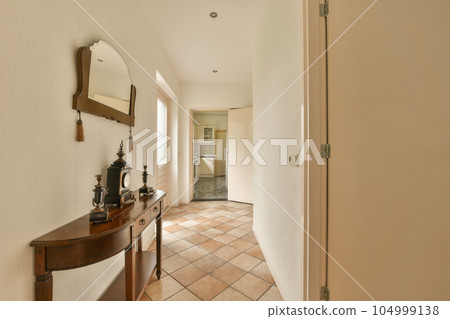 a hallway with a mirror on the wall and an open door leading to another room that has a tiled floor 104999138