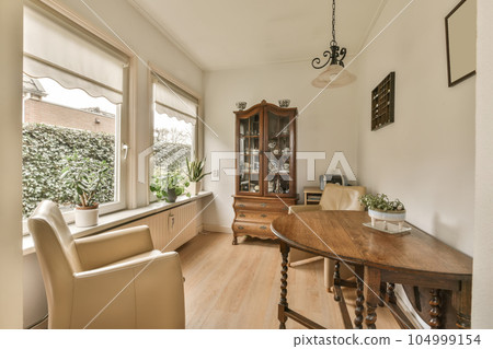 a dining room with wood flooring and white walls there is a large wooden table in front of the window 104999154