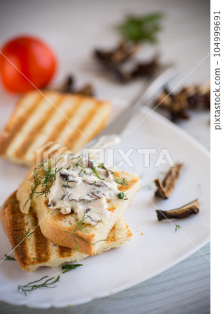 fried bread toast with cheese spread with boiled dried mushrooms on a wooden table. fried bread toast with cheese spread with boiled dried mushrooms on a wooden table. 104999691