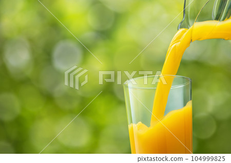 orange juice pouring into glass from jug on green background orange juice pouring into glass from jug on green background 104999825