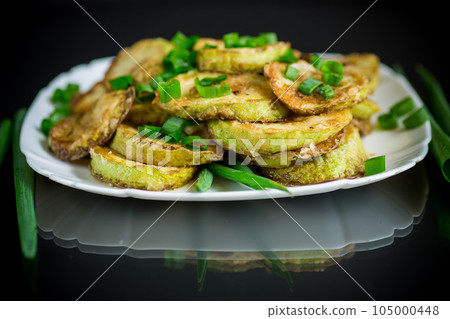 fried zucchini in circles with fresh herbs in a plate on a black 105000448