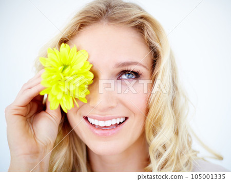 Beauty, makeup and female model with a flower in studio with a cosmetic, natural and face routine. Happy, smile and closeup of young woman with yellow floral spring plant isolated by white background Beauty, makeup and female model with a flower in studio with a cosmetic, natural and face routine. Happy, smile and closeup of young woman with yellow floral spring plant isolated by white background 105001335