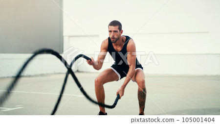 Man, fitness and battle rope exercise for physical training, workout or wellness in the outdoors. Fit, active and serious male person exercising with ropes for intense endurance, stamina or cardio 105001404