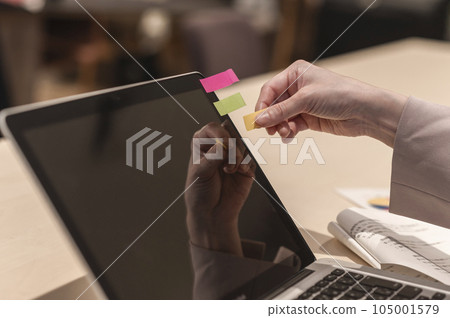 Woman's hand putting a sticky note on a laptop Woman's hand putting a sticky note on a laptop 105001579