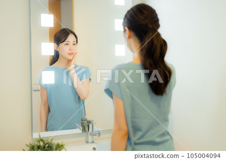 A woman looking at a mirror in the washroom 105004094