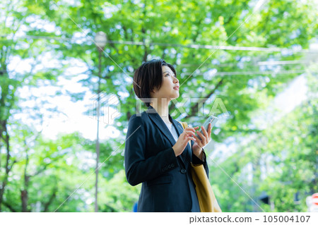 Woman in suit looking at smartphone outdoors 105004107