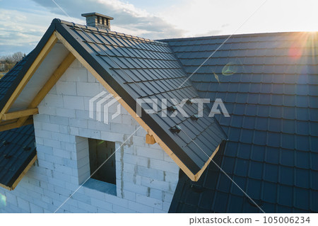 Aerial view of unfinished house with aerated lightweight concrete walls and wooden roof frame covered with metallic tiles under construction. Aerial view of unfinished house with aerated lightweight concrete walls and wooden roof frame covered with metallic tiles under construction. 105006234