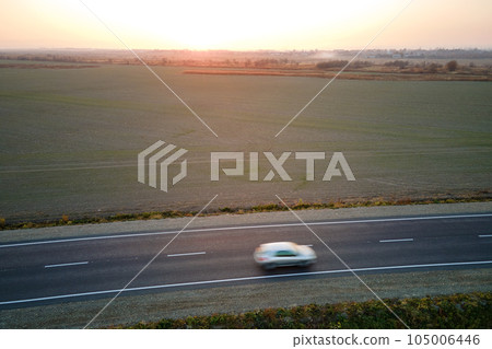 Aerial view of intercity road with blurred fast driving car at sunset. Top view from drone of highway traffic in evening Aerial view of intercity road with blurred fast driving car at sunset. Top view from drone of highway traffic in evening 105006446