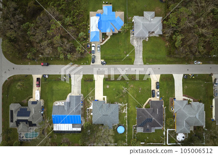 Aerial view of damaged in hurricane Ian house roof covered with blue protective tarp against rain water leaking until replacement of asphalt shingles 105006512