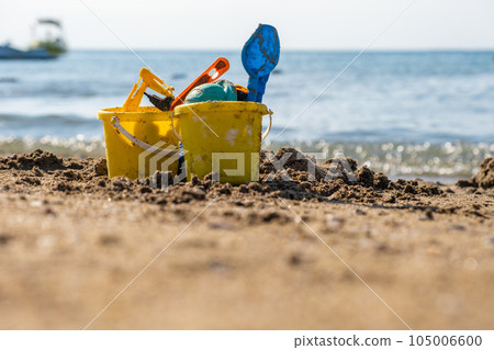 Children's beach toys - buckets, spade and shovel on sand on a sunny day. Bright toys on the background of the sea. 105006600