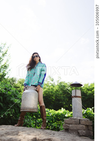 Young fashionable farmer woman posing on camera while holding milk can Young fashionable farmer woman posing on camera while holding milk can 105006997
