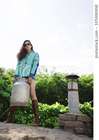 Young fashionable farmer woman posing on camera while holding milk can. Young fashionable farmer woman posing on camera while holding milk can. 105006998