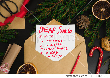 Letter to Santa Claus from Children on a Desk. Dear Santa. Top View of Child Wish List for Jolly Father. White Paper Page with Envelope on Wood Table with Christmas Ornament, Decorations, Sweet Candy. Letter to Santa Claus from Children on a Desk. Dear Santa. Top View of Child Wish List for Jolly Father. White Paper Page with Envelope on Wood Table with Christmas Ornament, Decorations, Sweet Candy. 105007106