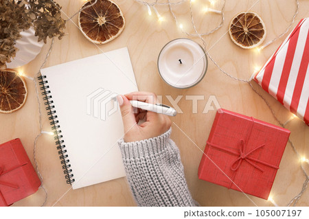 Christmas wish list writing. Woman creating present list for winter holidays. Top view, flat lay. Preparing for Xmas and New Year concept. Female hand writing in empty notebook on wooden table Christmas wish list writing. Woman creating present list for winter holidays. Top view, flat lay. Preparing for Xmas and New Year concept. Female hand writing in empty notebook on wooden table 105007197