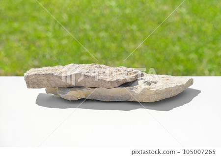Natural stone podium for presentation. Blurred green grass background. Abstract minimal backdrop. Two rock forms, sunlight. Scene to show. Showcase, display case. 3D Front View. Trendy summer color 105007265