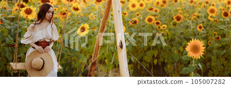 Woman in a dress in a field of sunflowers on a swing Woman in a dress in a field of sunflowers on a swing 105007282