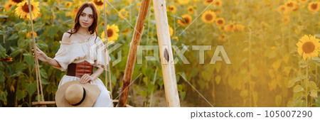 Woman in a dress in a field of sunflowers on a swing Woman in a dress in a field of sunflowers on a swing 105007290