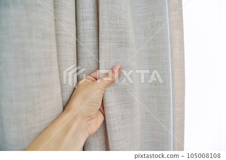Light beige sand linen natural curtains on window, close-up of hand touching curtains 105008108