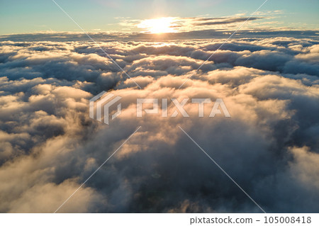 Aerial view from airplane window at high altitude of dense puffy cumulus clouds flying in evening Aerial view from airplane window at high altitude of dense puffy cumulus clouds flying in evening 105008418