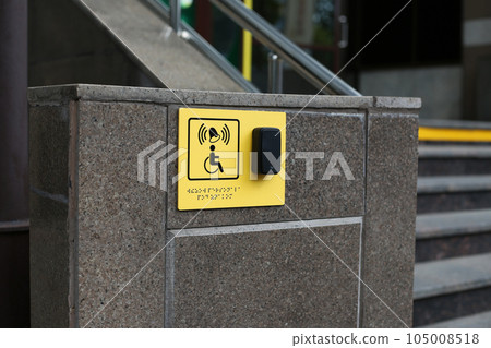 Yellow plate with image of disabled person in wheelchair and call button. Disabled person sign and panic button for help in front of the entrance to the building near the stairs, braille text 105008518