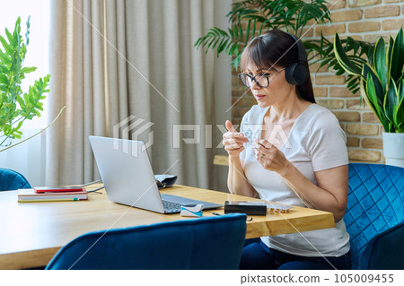 Mature woman in headphones having video chat with doctor, using laptop Mature woman in headphones having video chat with doctor, using laptop 105009455