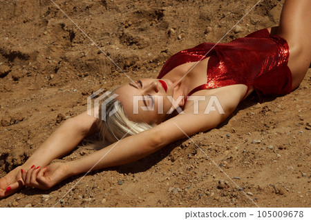 Beautiful blond woman in a red sexy dress on the background of the sky and sand. 105009678