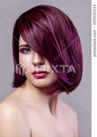 Portrait of beautiful fashion model woman with short purple colored hairstyle and makeup looking at camera with calm expression. Indoor studio shot isolated on gray background. Portrait of beautiful fashion model woman with short purple colored hairstyle and makeup looking at camera with calm expression. Indoor studio shot isolated on gray background. 105010114