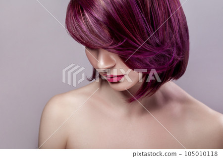 Side view portrait of calm beautiful attractive fashion model woman with short purple colored hairstyle and pink lips, looking down. Indoor studio shot isolated on gray background. 105010118