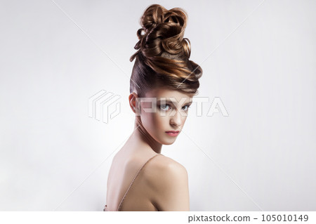 Portrait of attractive brunette young brown haired woman with stylish hairdo and makeup looking at camera with serious confident face. Indoor studio shot isolated on gray background. 105010149