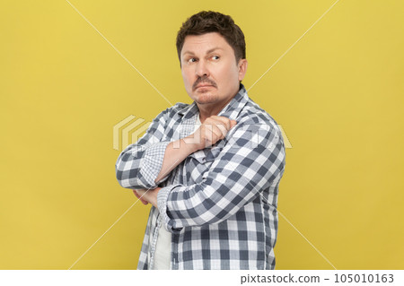Portrait of pensive handsome middle aged man in casual checkered shirt standing with thoughtful facial expression, looking away, thinking. Indoor studio shot isolated on yellow background. Portrait of pensive handsome middle aged man in casual checkered shirt standing with thoughtful facial expression, looking away, thinking. Indoor studio shot isolated on yellow background. 105010163