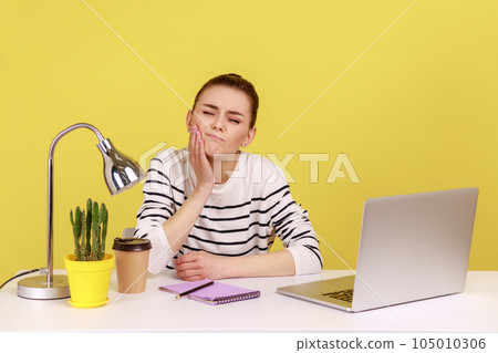 Unhealthy dissatisfied woman manager touching cheek feeling pain and discomfort in oral cavity, toothache and gums inflammation. Indoor studio studio shot isolated on yellow background. Unhealthy dissatisfied woman manager touching cheek feeling pain and discomfort in oral cavity, toothache and gums inflammation. Indoor studio studio shot isolated on yellow background. 105010306