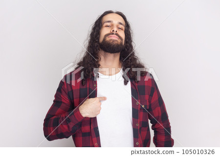 This is me. Satisfied proud bearded man in checkered red shirt points at himself, stands self confident, feels successful of his own achievement. Indoor studio shot isolated on gray background. 105010326
