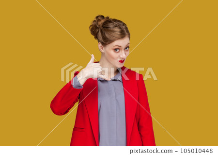 Portrait of flirting positive woman with red lips standing showing call me back gesture, looking at camera, wearing red jacket. Indoor studio shot isolated on yellow background. Portrait of flirting positive woman with red lips standing showing call me back gesture, looking at camera, wearing red jacket. Indoor studio shot isolated on yellow background. 105010448