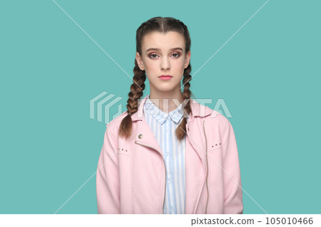 Portrait of serious strict young teenager girl with braids wearing pink jacket looking at camera with bossy expression, being in bad mood. Indoor studio shot isolated on green background. Portrait of serious strict young teenager girl with braids wearing pink jacket looking at camera with bossy expression, being in bad mood. Indoor studio shot isolated on green background. 105010466