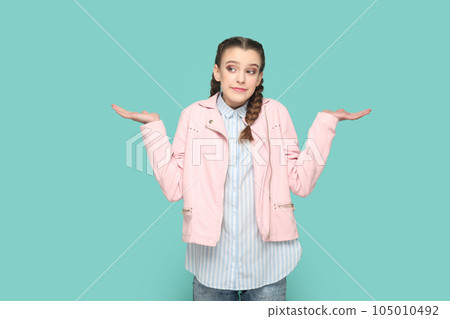 Portrait of uncertain confused teenager girl with braids wearing pink jacket standing shrugging shoulders, spread hands, don't know answer. Indoor studio shot isolated on green background. Portrait of uncertain confused teenager girl with braids wearing pink jacket standing shrugging shoulders, spread hands, don't know answer. Indoor studio shot isolated on green background. 105010492