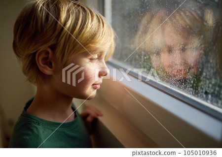 Portrait of preteen boy standing at the window. Child watching the rain outside. 105010936