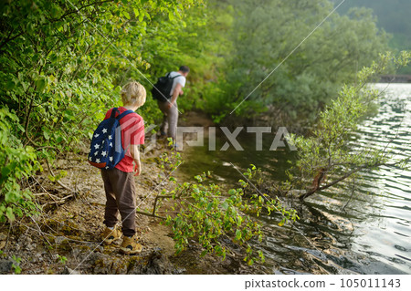 School child boy and father are hiking along forest lake and exploring nature. Family traveling in woodland. Summer vacation activity for inquisitive kids. Adventure, scouting, tourism for children 105011143