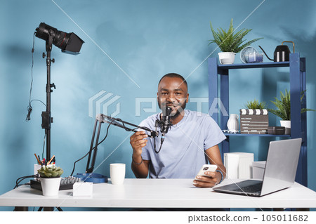 Smiling blogger reading engaging content on smartphone and looking at camera while recording video. Cheerful man sharing fun news and holding mobile phone while streaming live portrait 105011682